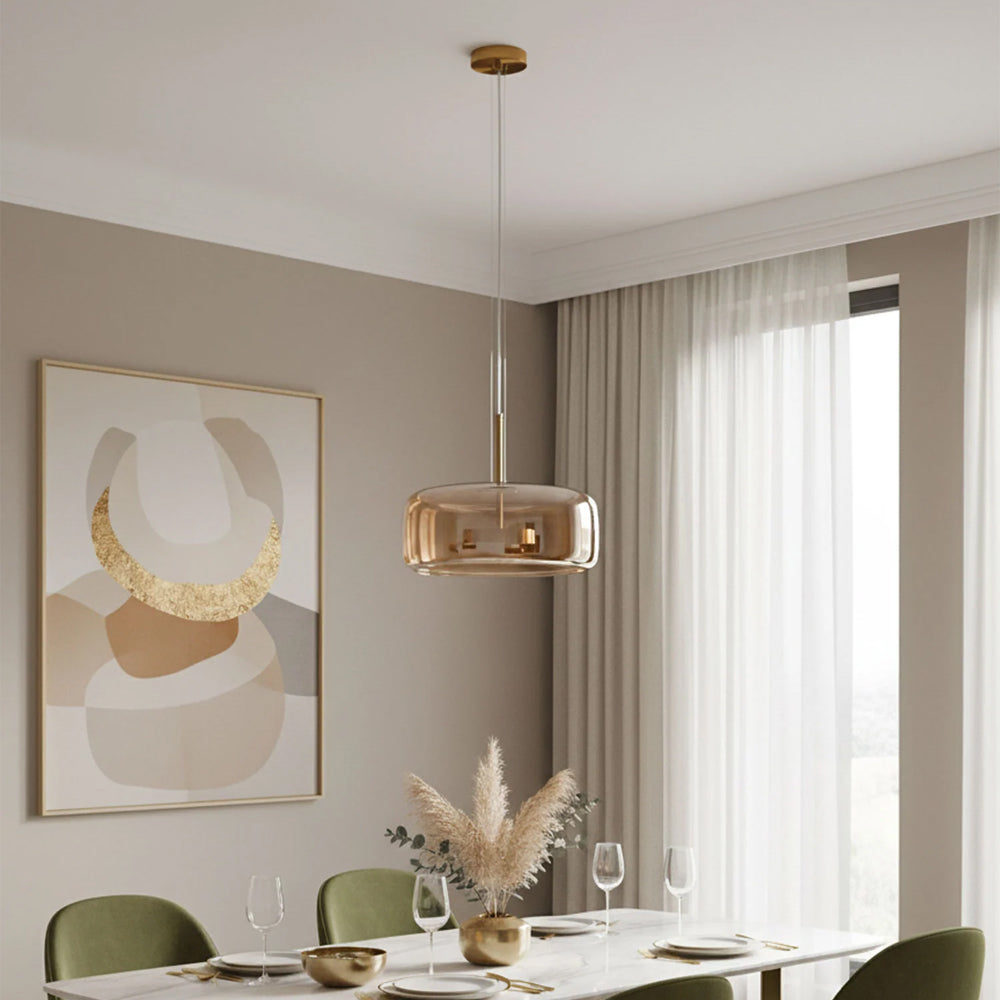 Nordic Glow Smoked Glass LED Pendant Light in amber, illuminating a modern dining room with an abstract painting, white marble table, and green velvet chairs. A minimalist and contemporary lighting fixture.