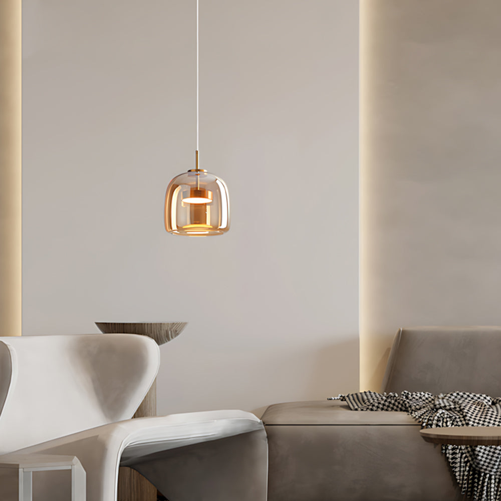 Nordic Glow A-shape amber smoked glass LED pendant light with warm glow, hanging in a modern living room above a grey sofa and white chair, showcasing minimalist design and ambient lighting.