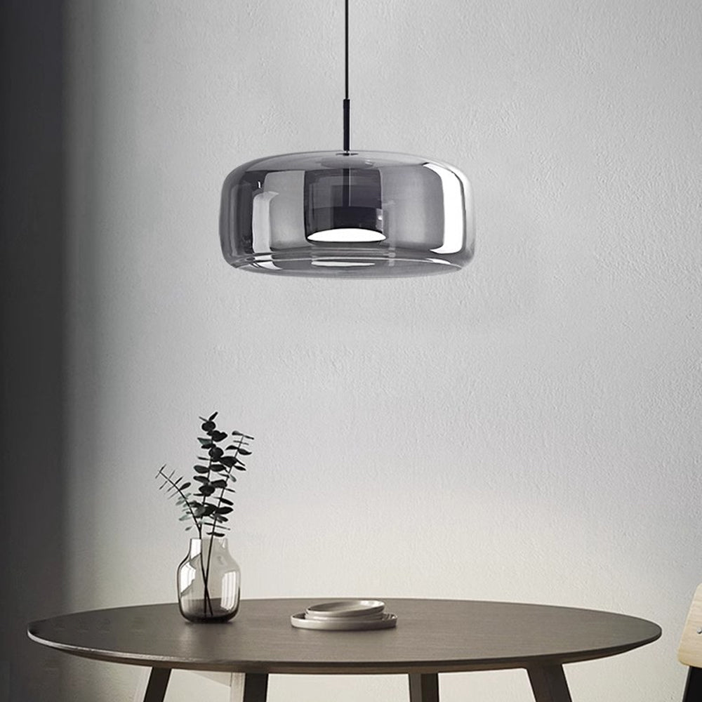 Nordic Glow B-shape grey smoked glass LED pendant light with white light, hanging above a round wooden dining table with a minimalist plant, showcasing its modern industrial style.