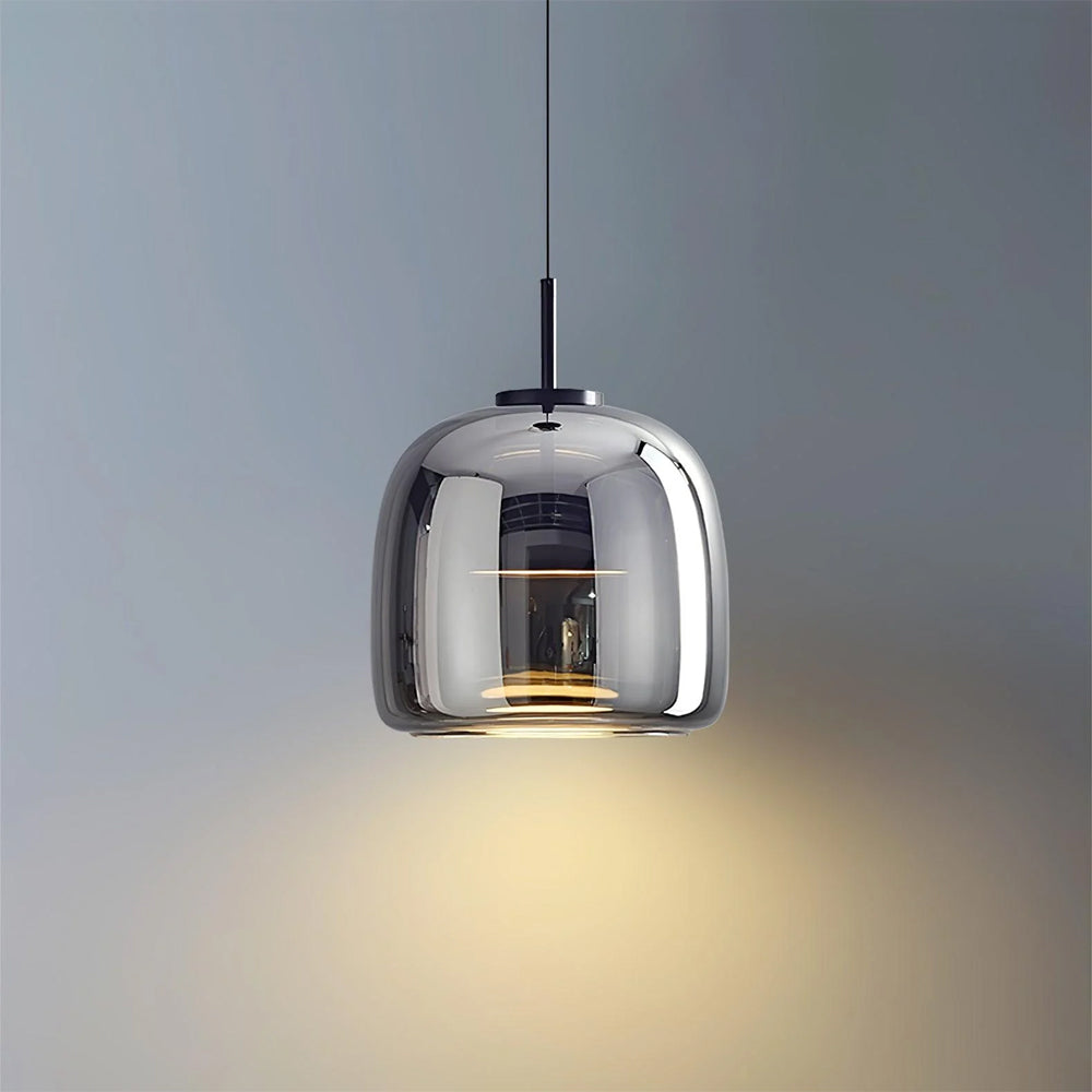 A single Nordic Glow smoked glass LED pendant light in grey, illuminated with a warm glow, hanging against a plain grey wall, highlighting its modern minimalist design.