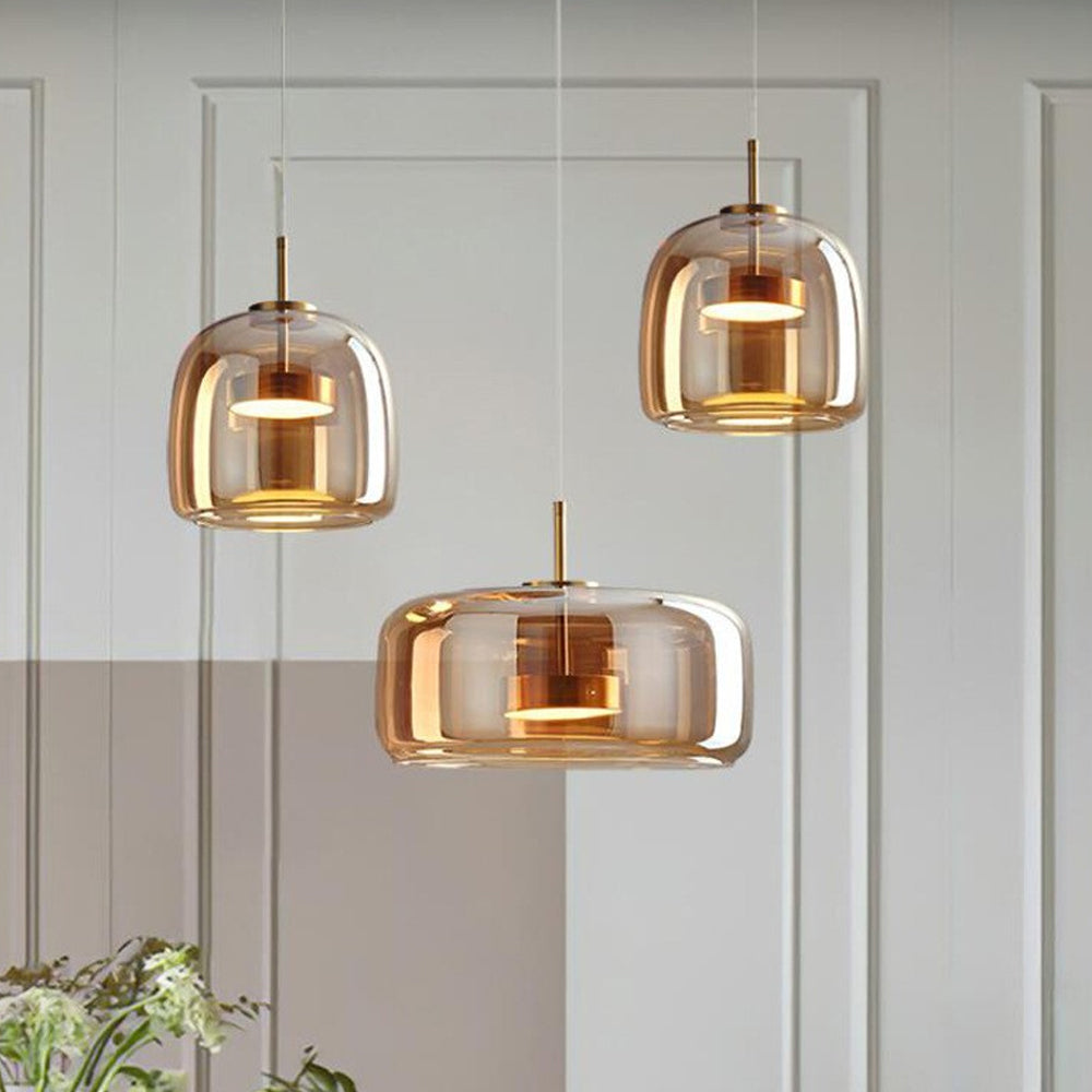Three Nordic Glow Smoked Glass LED Pendant Lights, two type A and one type B, in amber, hanging at varying heights against a light wall with paneling. Modern ambient lighting.