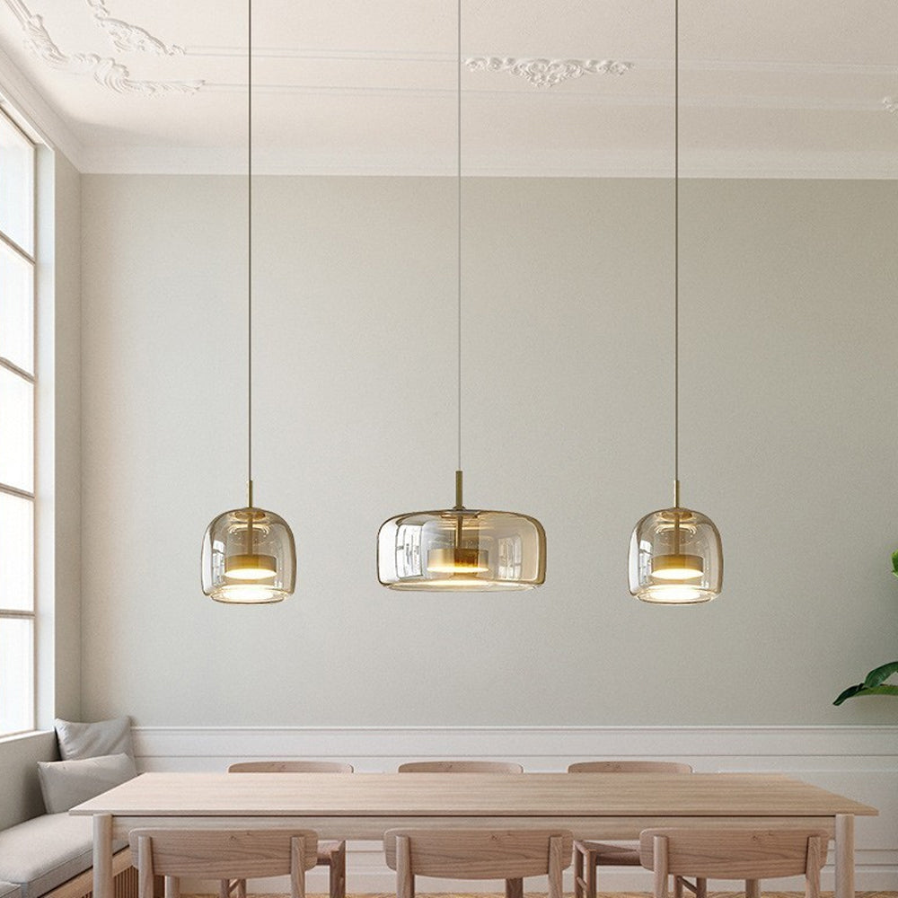 Three Nordic Glow Smoked Glass LED Pendant Lights, two type A and one type B, in amber, hanging above a wooden dining table with chairs in a minimalist dining room. Contemporary dining lighting.