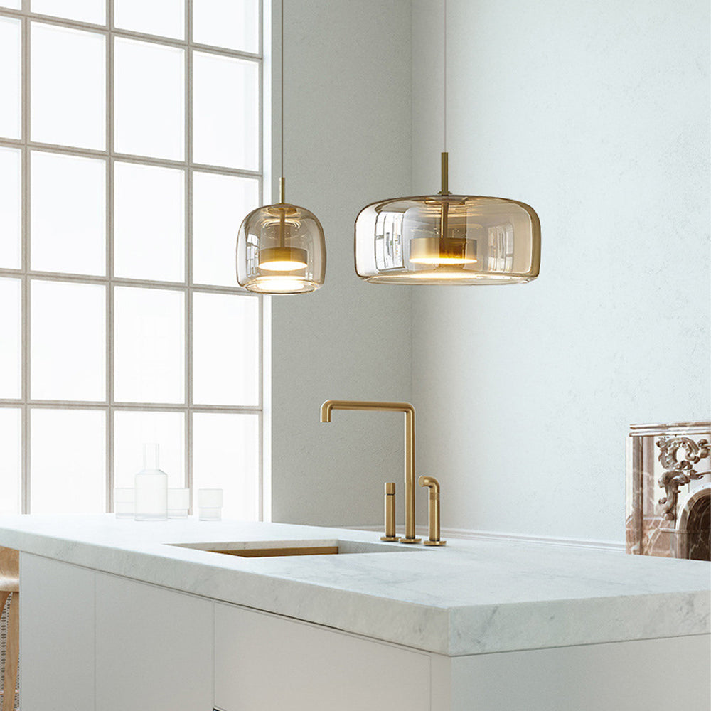 Two Nordic Glow Smoked Glass LED Pendant Lights, one type A and one type B, in amber, hanging above a modern kitchen counter with a gold faucet and large window. Minimalist kitchen lighting.
