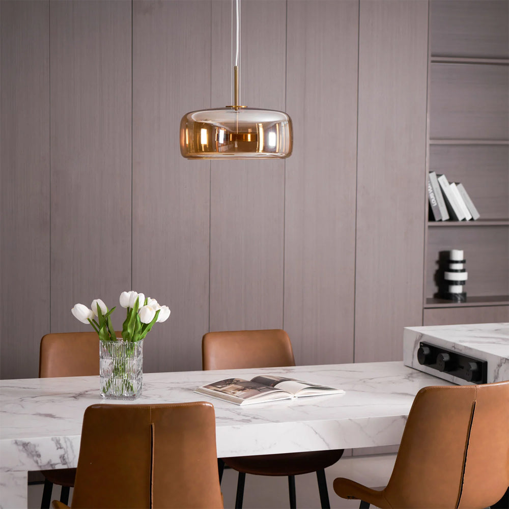 Nordic Glow smoked glass LED pendant light with minimalist design, featuring an amber glass shade, hanging in a modern dining room with a marble table, brown leather chairs, and white tulips.