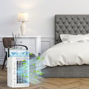 BreezeCraft Portable Air Conditioner Mini Cooler in a bedroom, placed on a wooden floor next to a bed and bedside table with a lamp. The cooler emits a blue light and green leaves, symbolizing cool, refreshing air. Ideal for personal cooling and summer comfort.