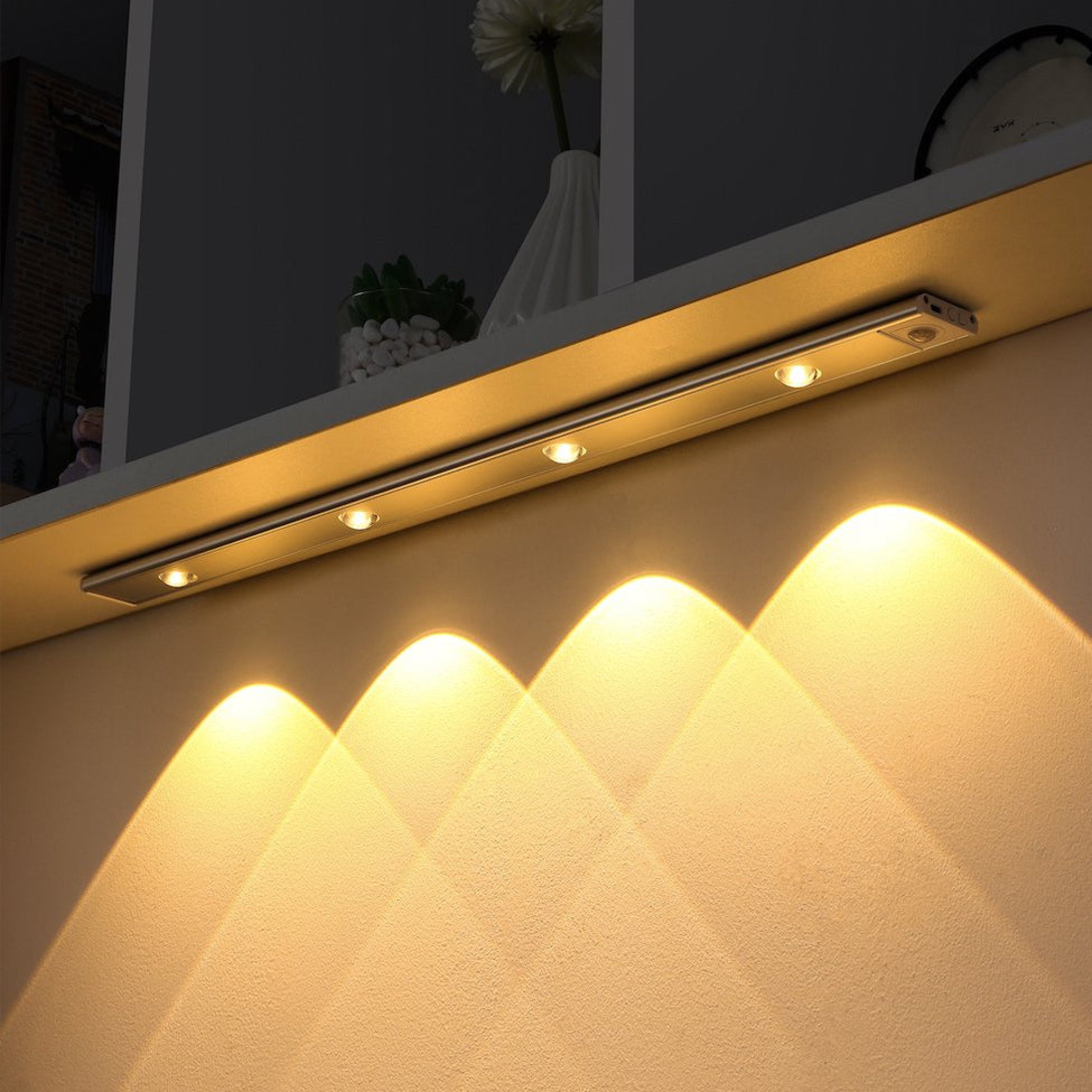 Sora Motion Sensor LED Lamp with Ambient Light Diffuser installed under a shelf, illuminating a wall with warm, soft light. Five individual LED lights are visible.