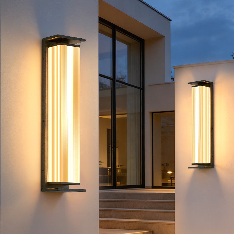 Three-quarter angle view of stainless steel vertical ribbed waterproof LED outdoor wall sconce glowing warm light mounted on rustproof outdoor column