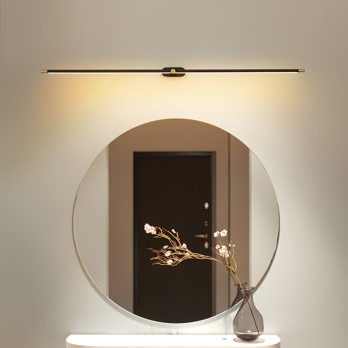 Vestra Minimalist Linear Rechargeable Wall Lamp in black metal with LED finish, mounted above a round mirror with a vase of pink flowers on a console table, emitting a warm glow.