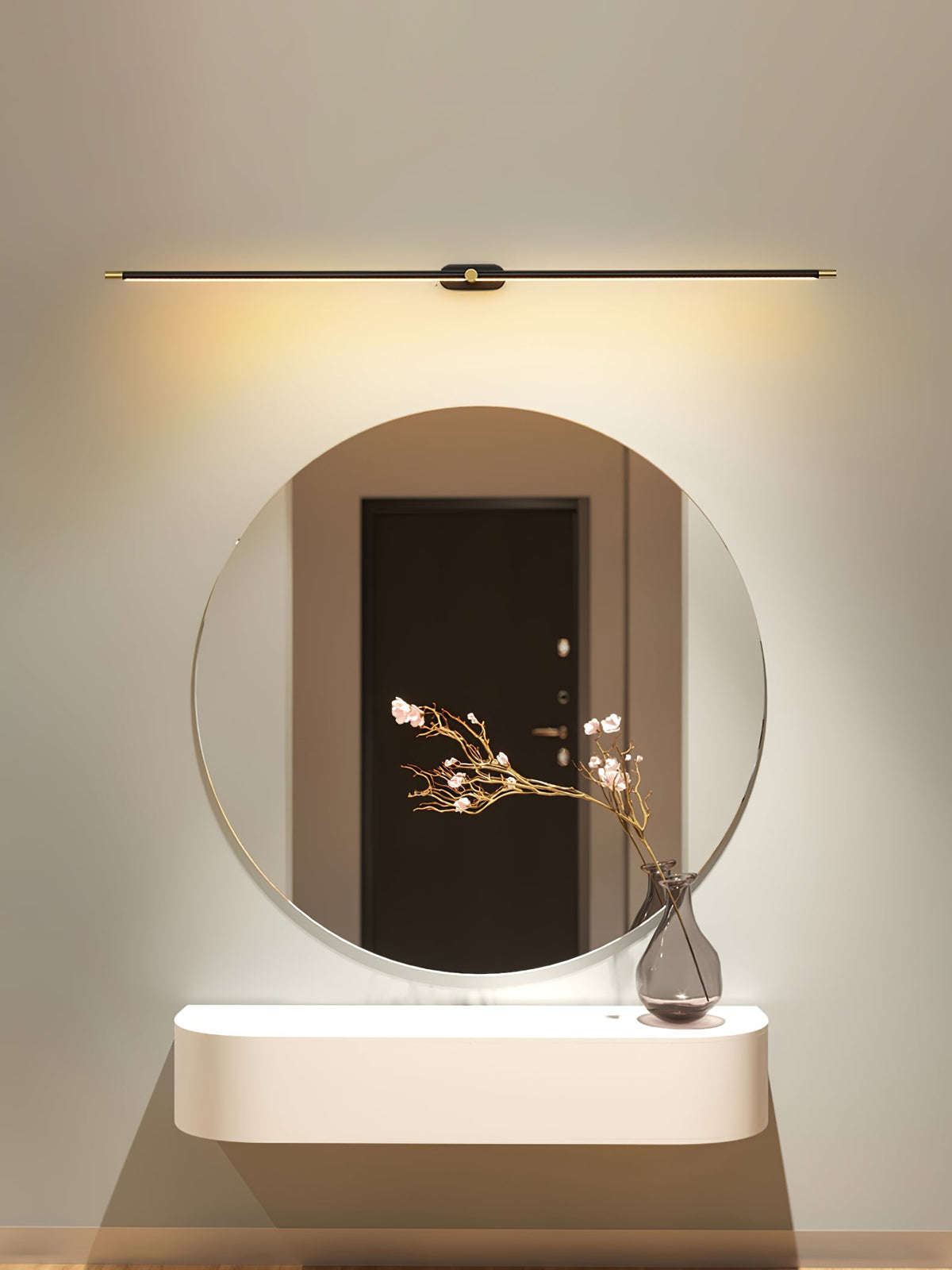 Vestra Minimalist Linear Rechargeable Wall Lamp in black metal with LED finish, mounted above a round mirror with a vase of pink flowers on a console table, emitting a warm glow.