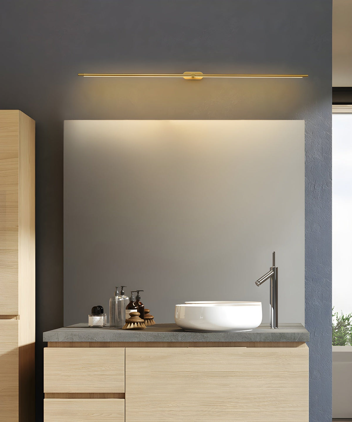 Vestra Minimalist Linear Rechargeable Wall Lamp in gold finish, mounted above a large mirror in a modern bathroom with a wooden vanity and white sink.