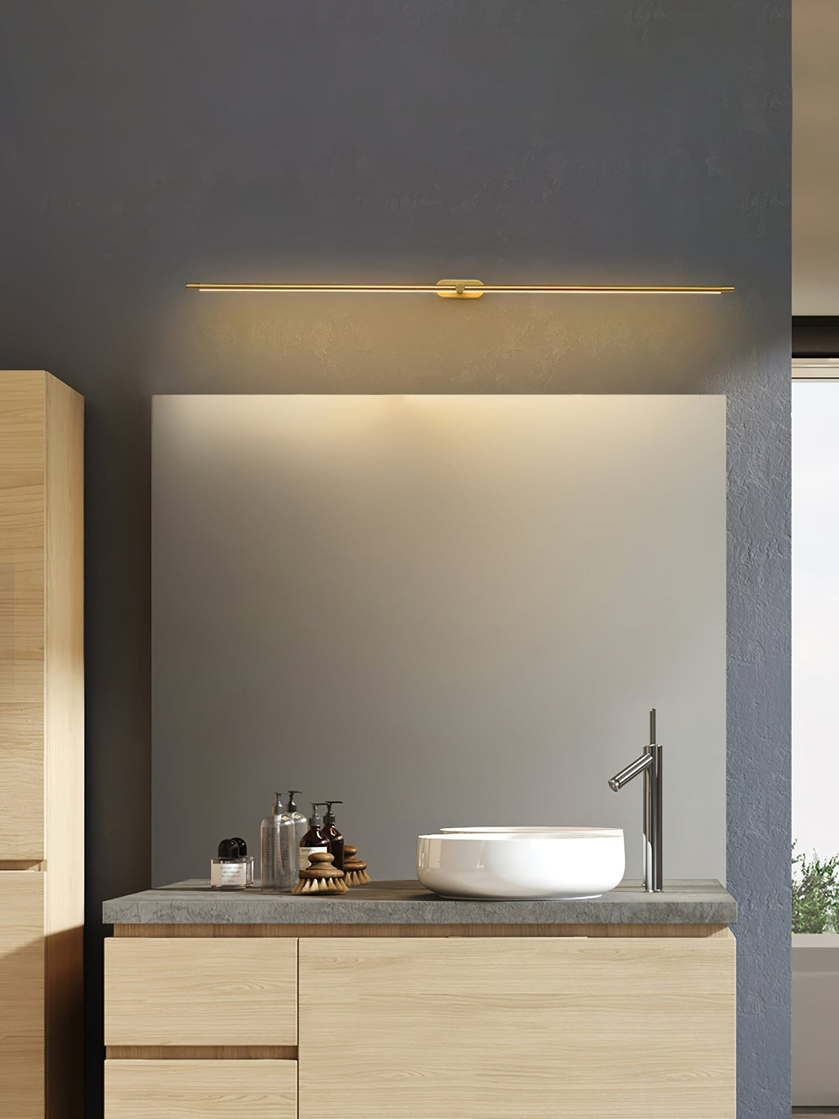 Vestra Minimalist Linear Rechargeable Wall Lamp in gold metal with LED finish, installed above a rectangular mirror in a modern bathroom vanity with a white basin and faucet.