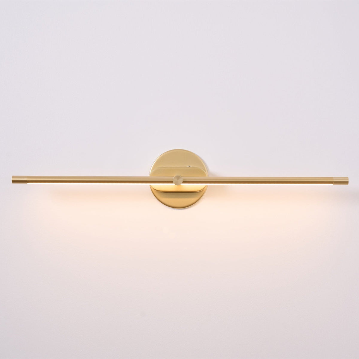 A Vestra Minimalist Linear Rechargeable Wall Lamp in gold finish, illuminated with a warm LED light, featuring a sleek linear design a circular mounting base, presented against a plain white background.