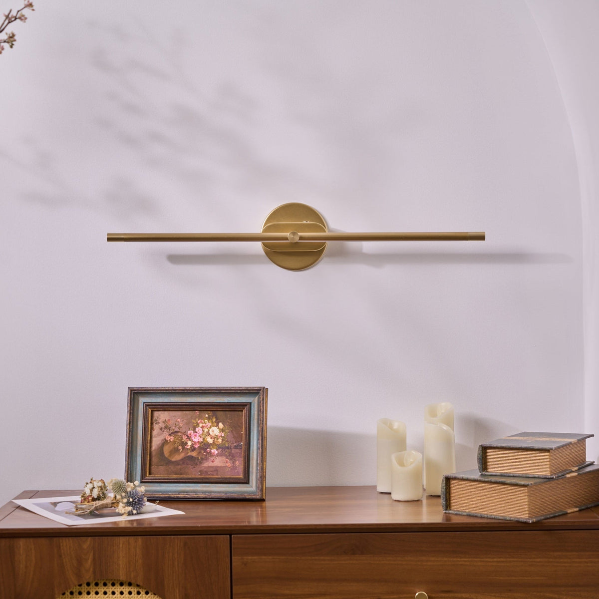 Vestra Minimalist Linear Rechargeable Wall Lamp Metal LED Finish in gold, not illuminated, mounted above a wooden dresser with a framed floral picture.