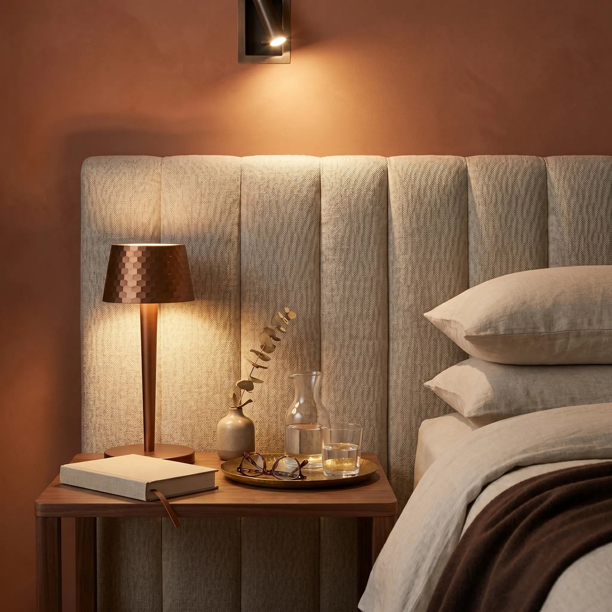 Aluminum touch dimmable USB rechargeable LED bedside lamp at three-quarter angle in brushed aluminum lit on hotel bedside with terracotta wall